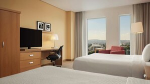 A hotel room with two beds, a desk with a chair, a television, and a large window offering a city view. - Courtyard by Marriott Leon at the Poliforum (León)