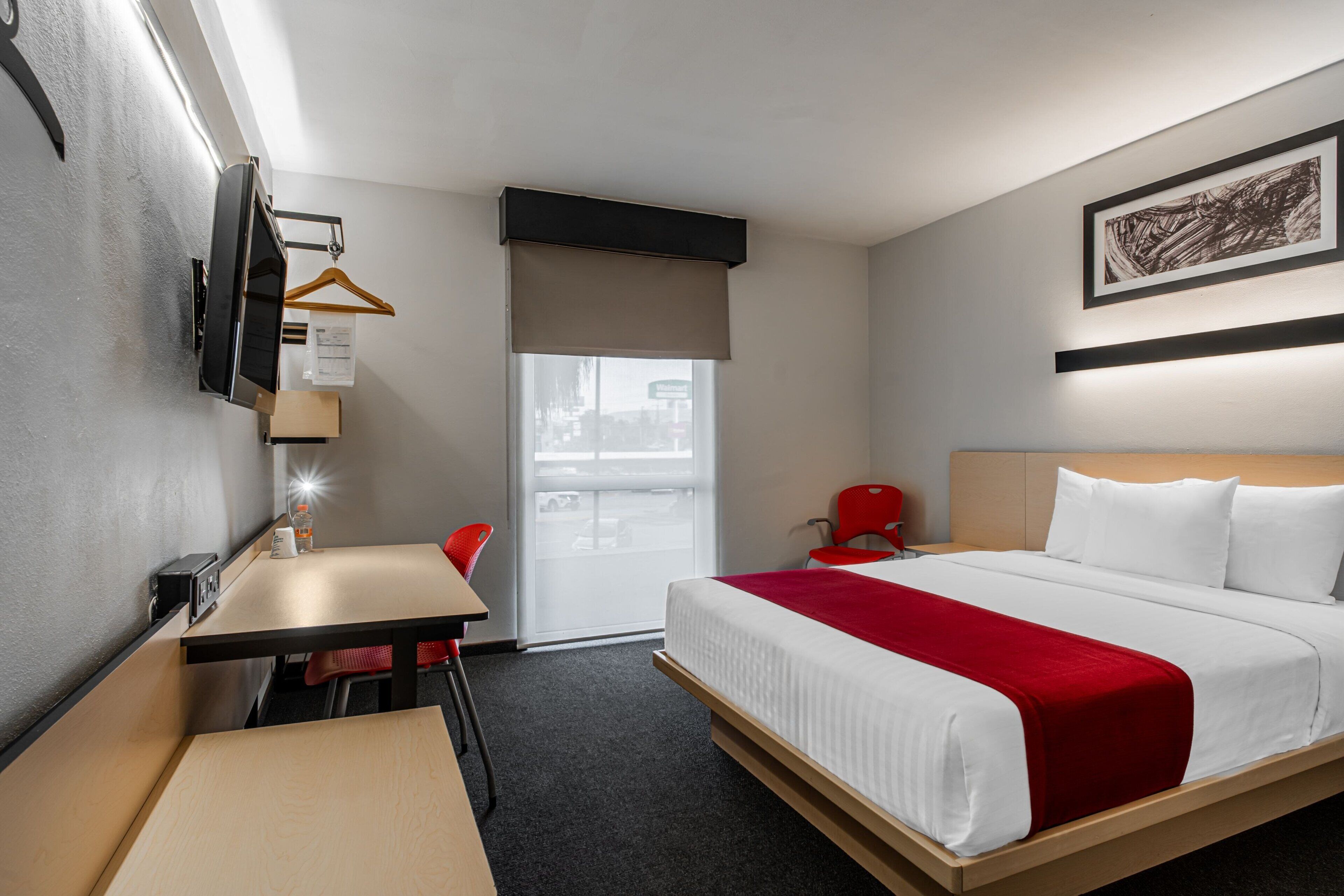 A hotel room with a bed, a desk, a chair, a window, and a door.
