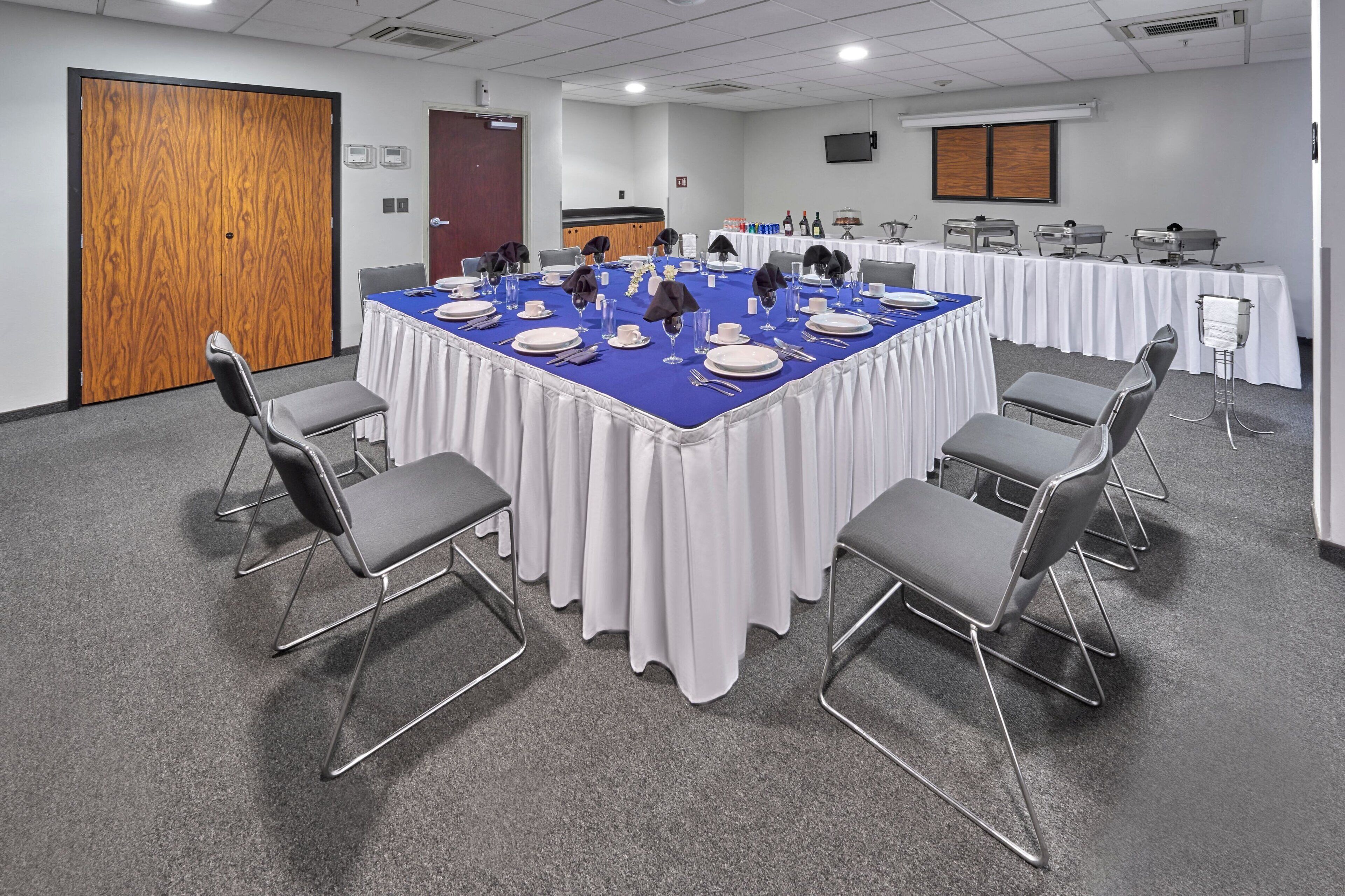A conference room with a large table set for a meeting, surrounded by chairs, and a wooden door in the background.