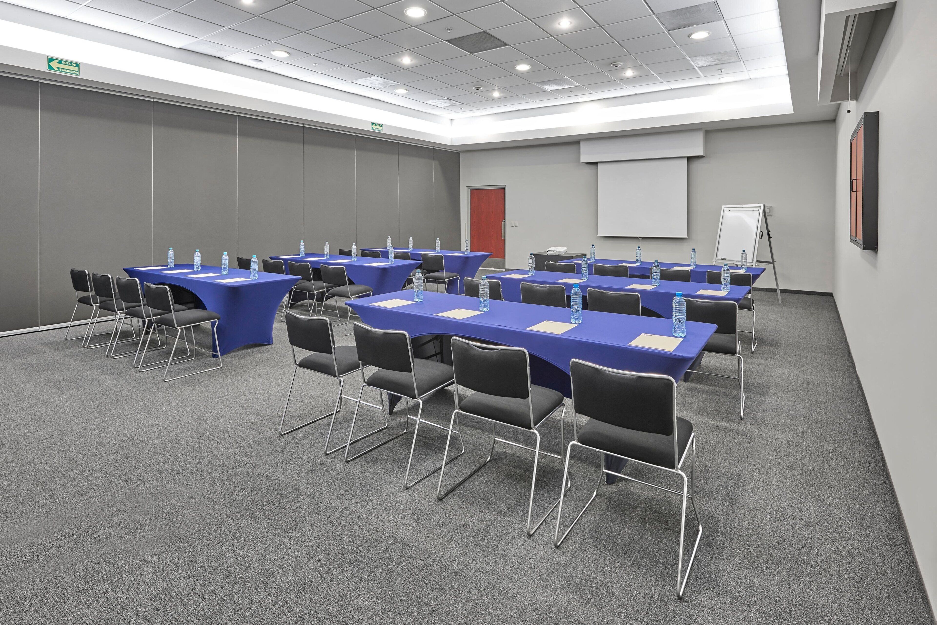 Un salón de conferencias con varias mesas, sillas y botellas de agua.