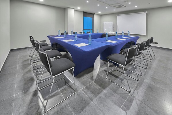Una sala de conferencias con una gran mesa, sillas, botellas de agua y una pizarra.