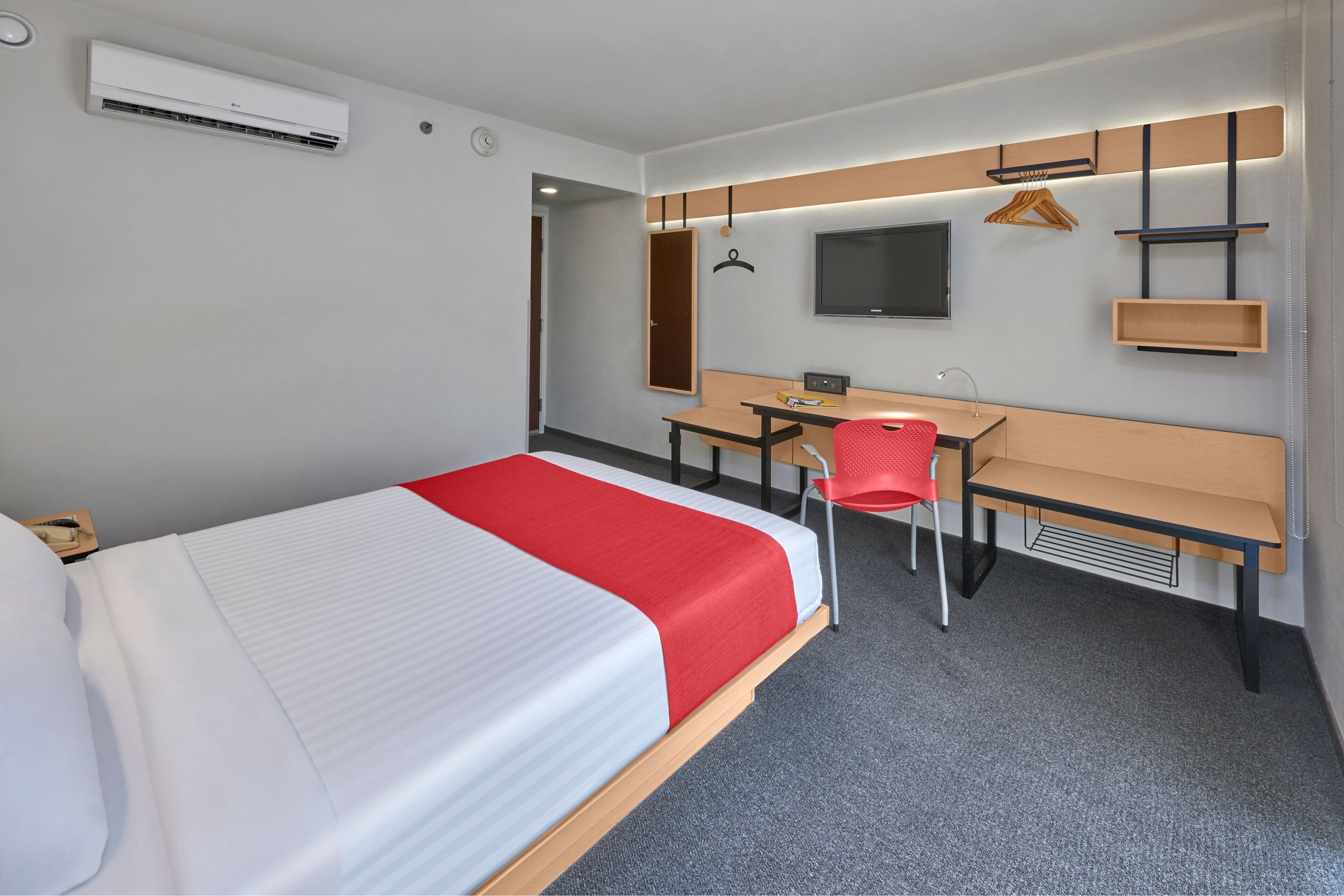 A hotel room with a bed, a desk, a chair, a TV, and a wardrobe.