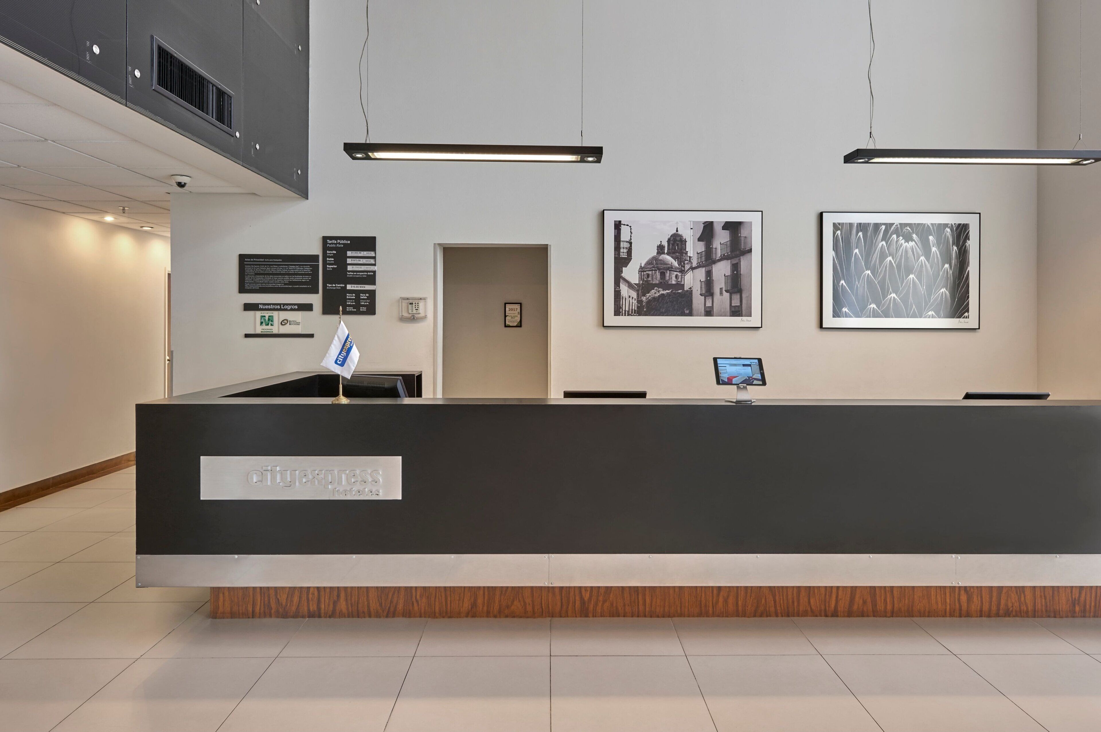A reception desk with a sign reading "cityexpress," a digital screen, framed artwork, and a door to the left.