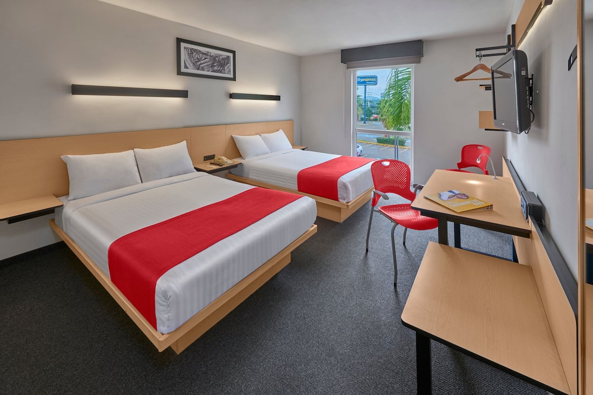 A hotel room with two beds, a desk, a chair, and a TV.