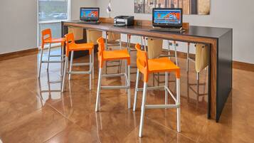 Zona de bar moderna con una barra alargada, varias sillas color naranja y dos computadoras portátiles sobre la barra.