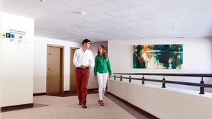 Een hal met een modern ontwerp, met een houten deur waarop '255' staat, een glazen balustrade en een kleurrijk abstract schilderij aan de muur.