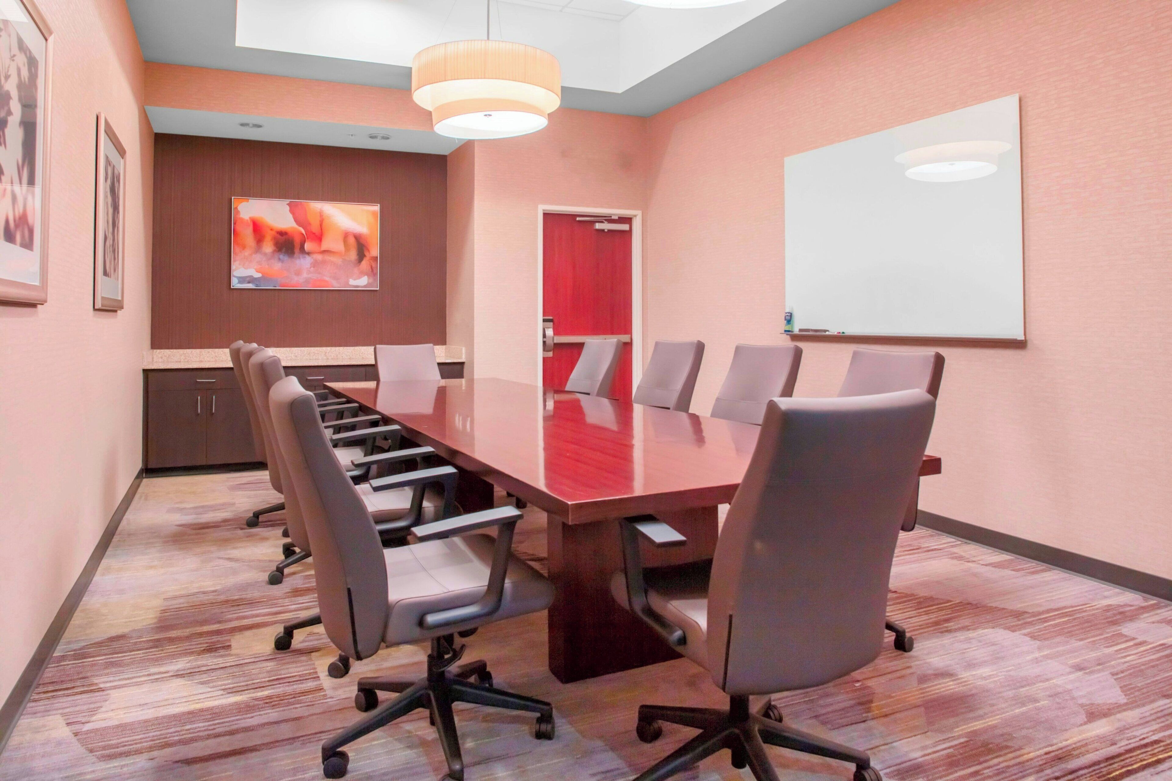 A conference room with a long table, six chairs, and a whiteboard on the wall.