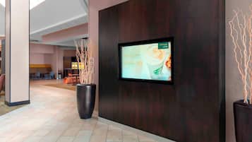 A modern lobby with a digital screen displaying a Starbucks advertisement, a large planter, and a seating area in the background.