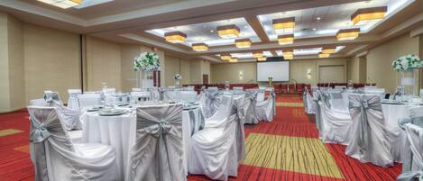 A conference room with round tables, each covered with white tablecloths and silver sashes, and chairs with white covers and silver sashes.