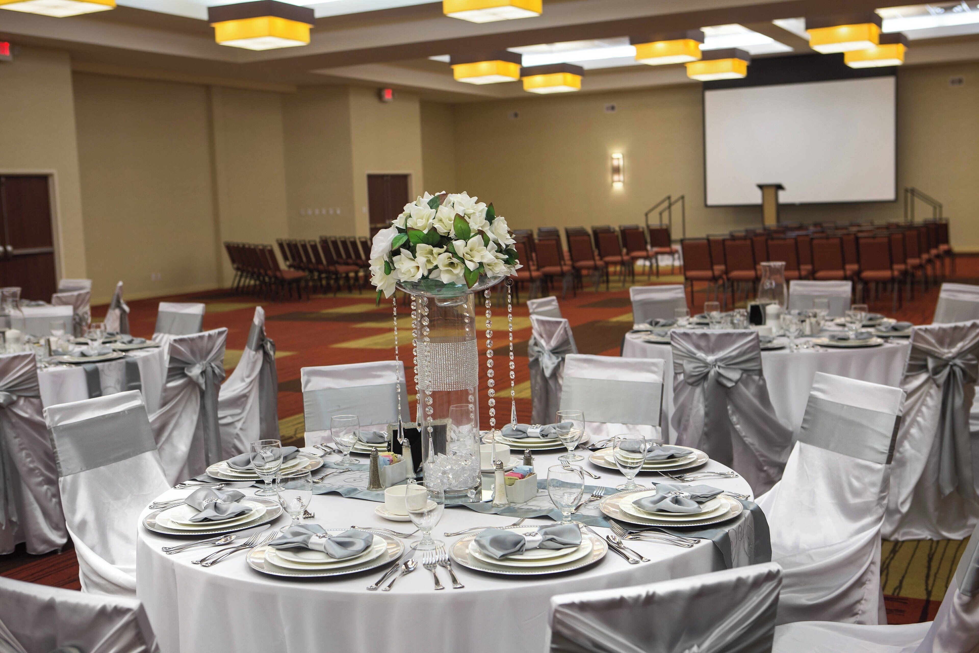 A banquet hall with round tables set for a formal event, featuring white tablecloths and silver sashes.