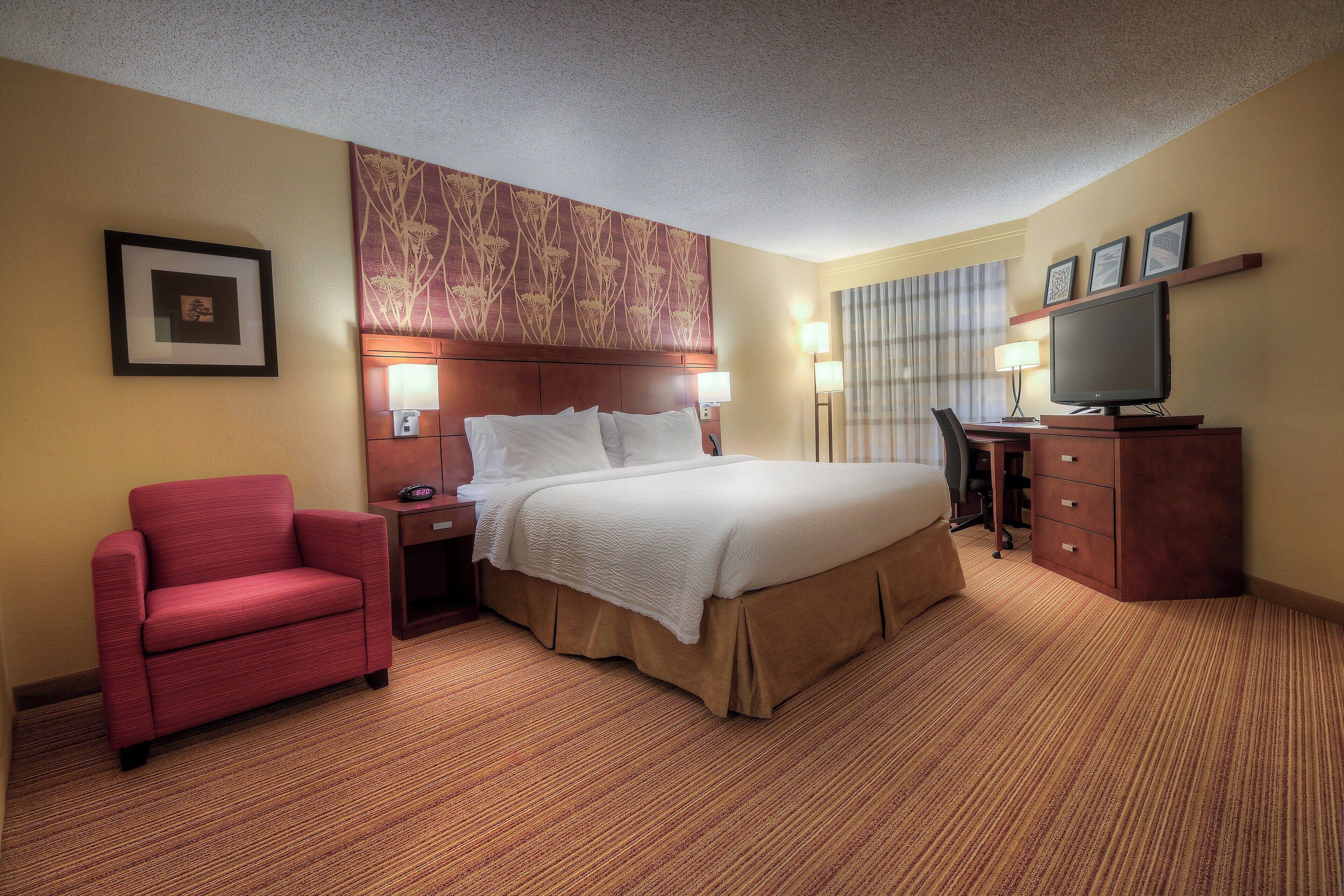 A hotel room with a bed, a desk, a chair, and a TV.