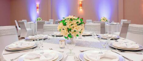 A banquet hall with round tables set for a formal event, featuring white tablecloths, silverware, and floral centerpieces.
