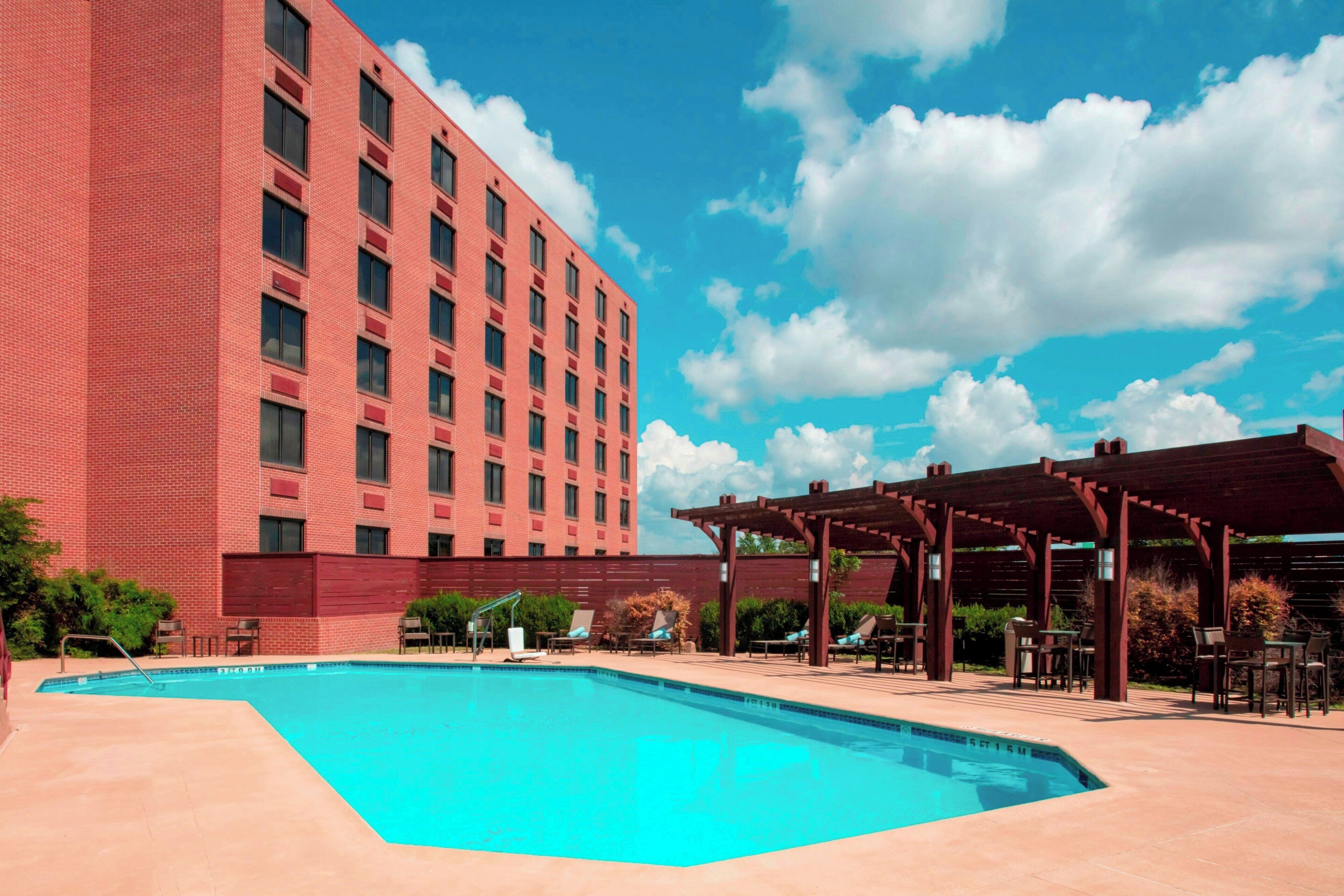 A swimming pool with lounge chairs and a covered seating area, adjacent to a red brick building.