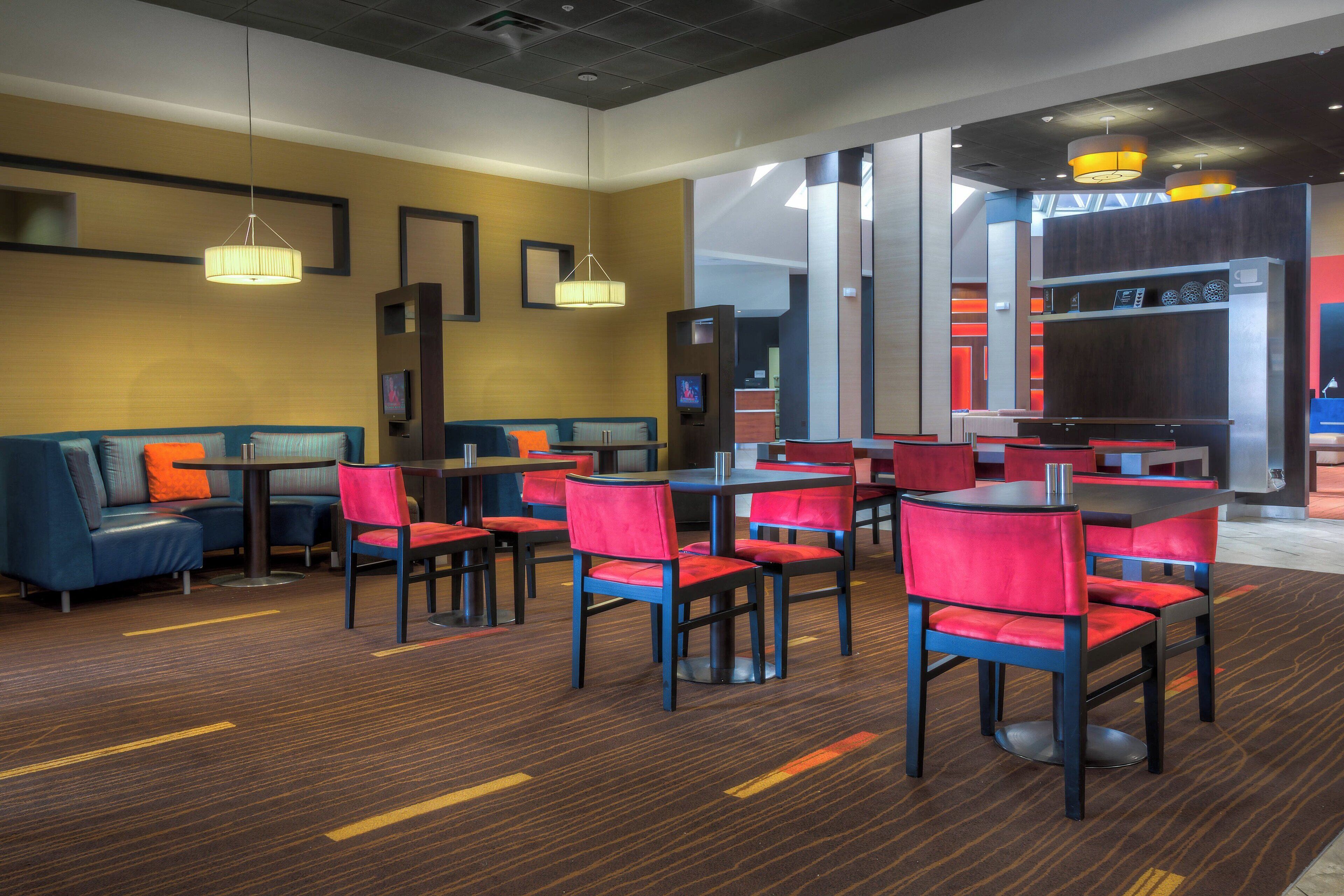 A modern hotel lobby with seating areas, a television, and a kitchen area.