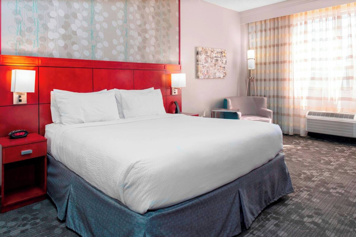 A hotel room with a large bed, two bedside tables, a chair, and a window with curtains.