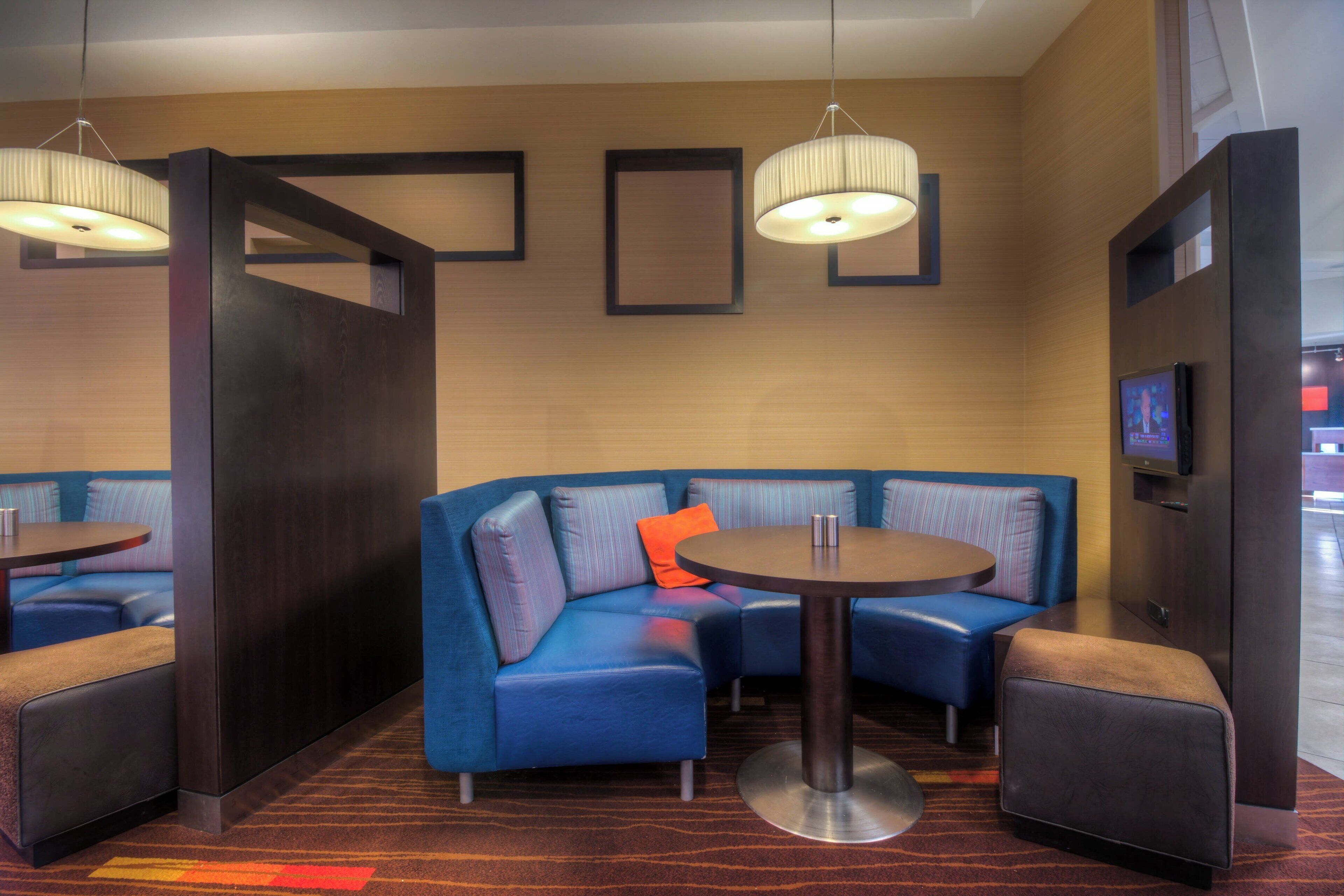 A modern hotel room with a sectional sofa, a round table, and two pendant lights.