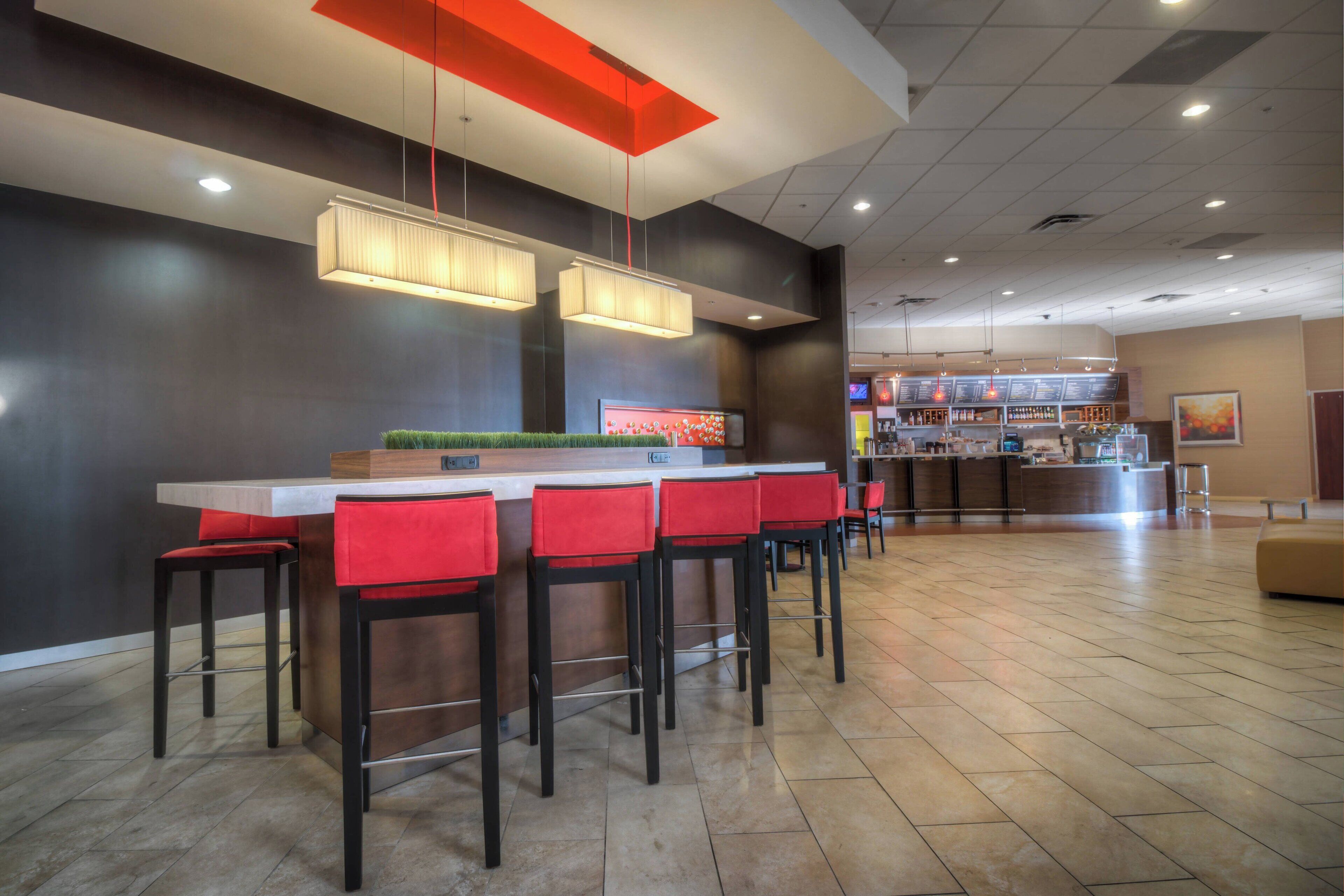 A modern bar area with a long counter, multiple red bar stools, and pendant lighting.