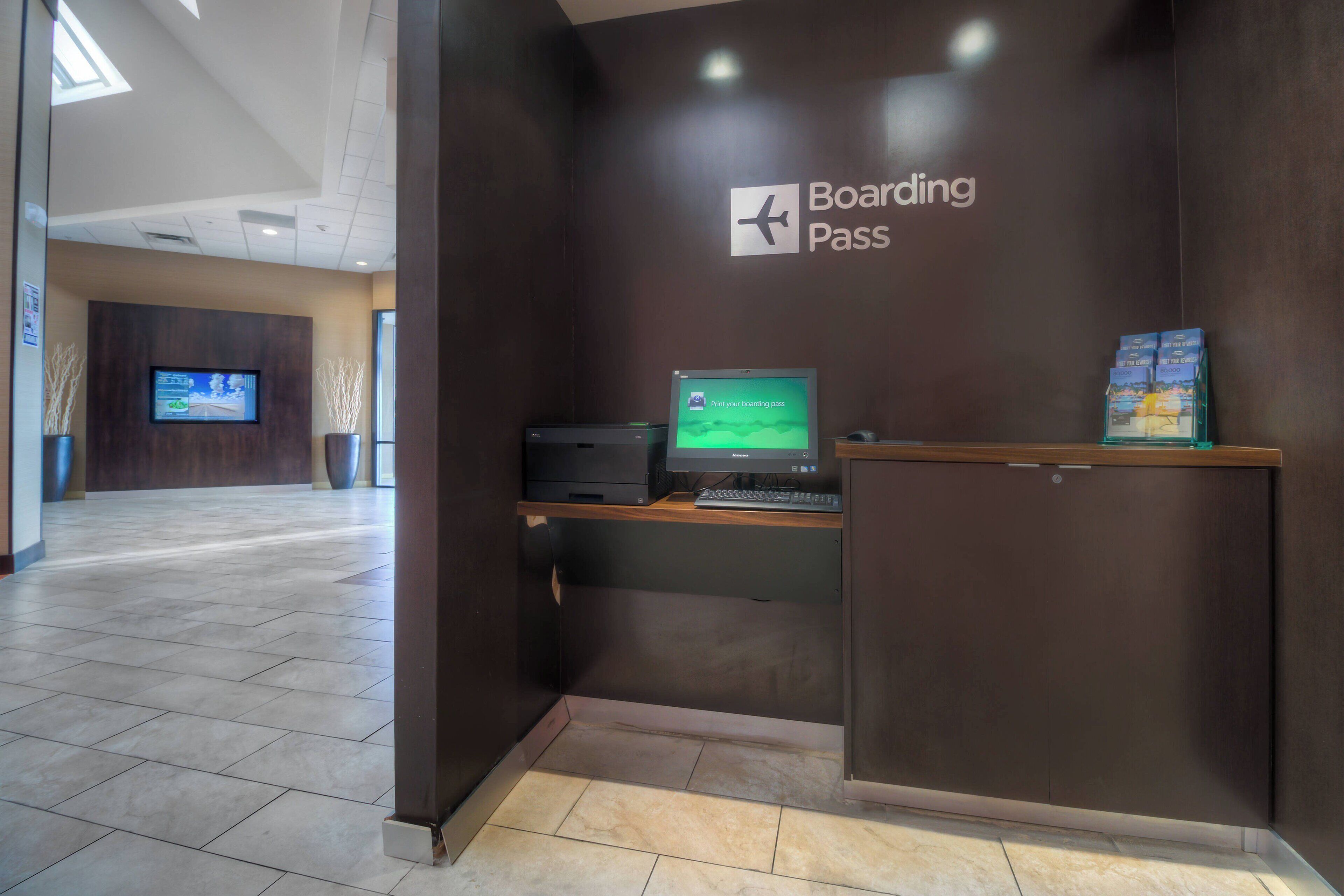 A modern check-in area with a digital display for boarding passes, a flat-screen TV, and a wooden desk.