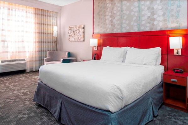 Una habitación de hotel con una cama grande, un escritorio, una silla y una lámpara de pared.