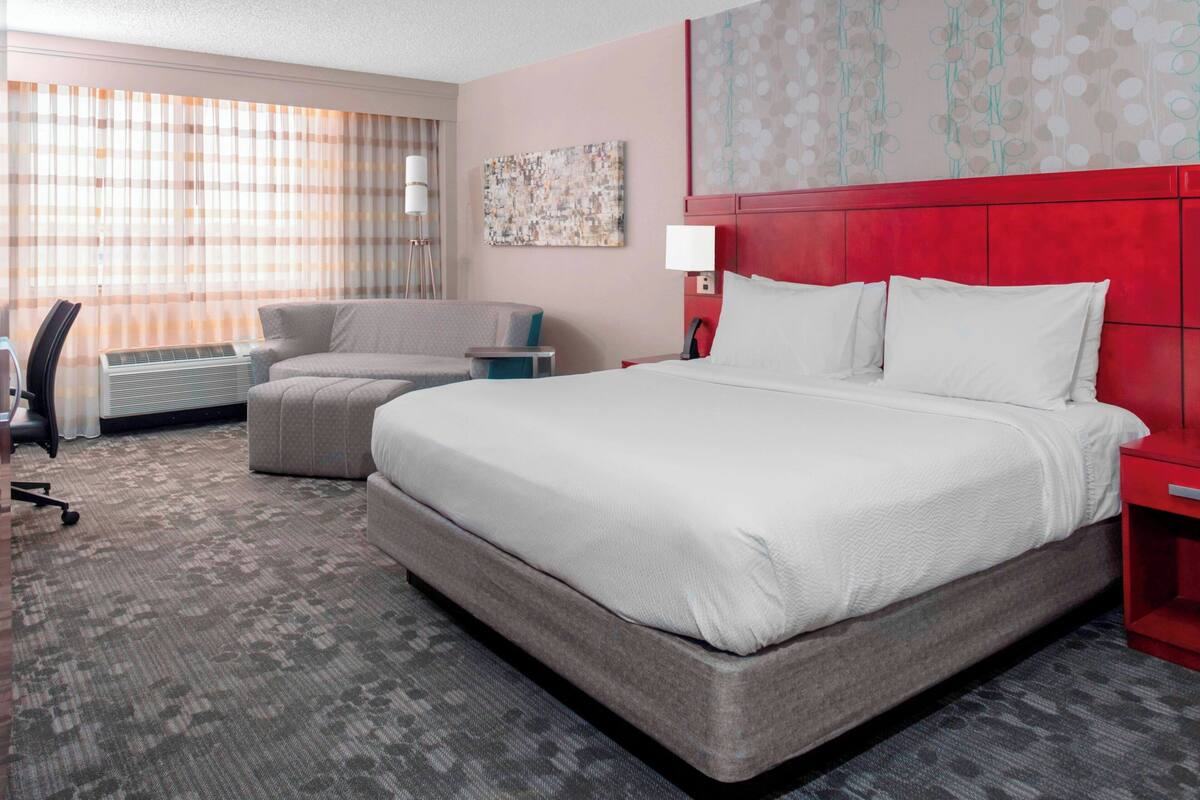 A hotel room with a large bed, a desk, a chair, and a window with curtains.