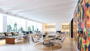 A spacious, modern lounge area with a long bench, multiple seating options, and a large bookshelf in the background.