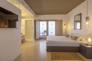 A modern hotel room with a large bed, bedside tables, a mirror, and a view of the outside through a door.
