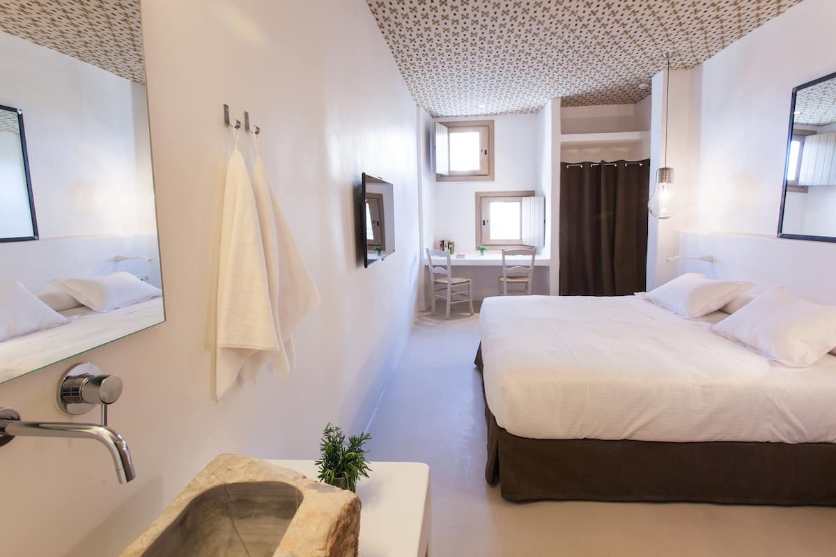 Une chambre d’hôtel avec un grand lit, un bureau et une salle de bain équipée d’un lavabo et d’un miroir.