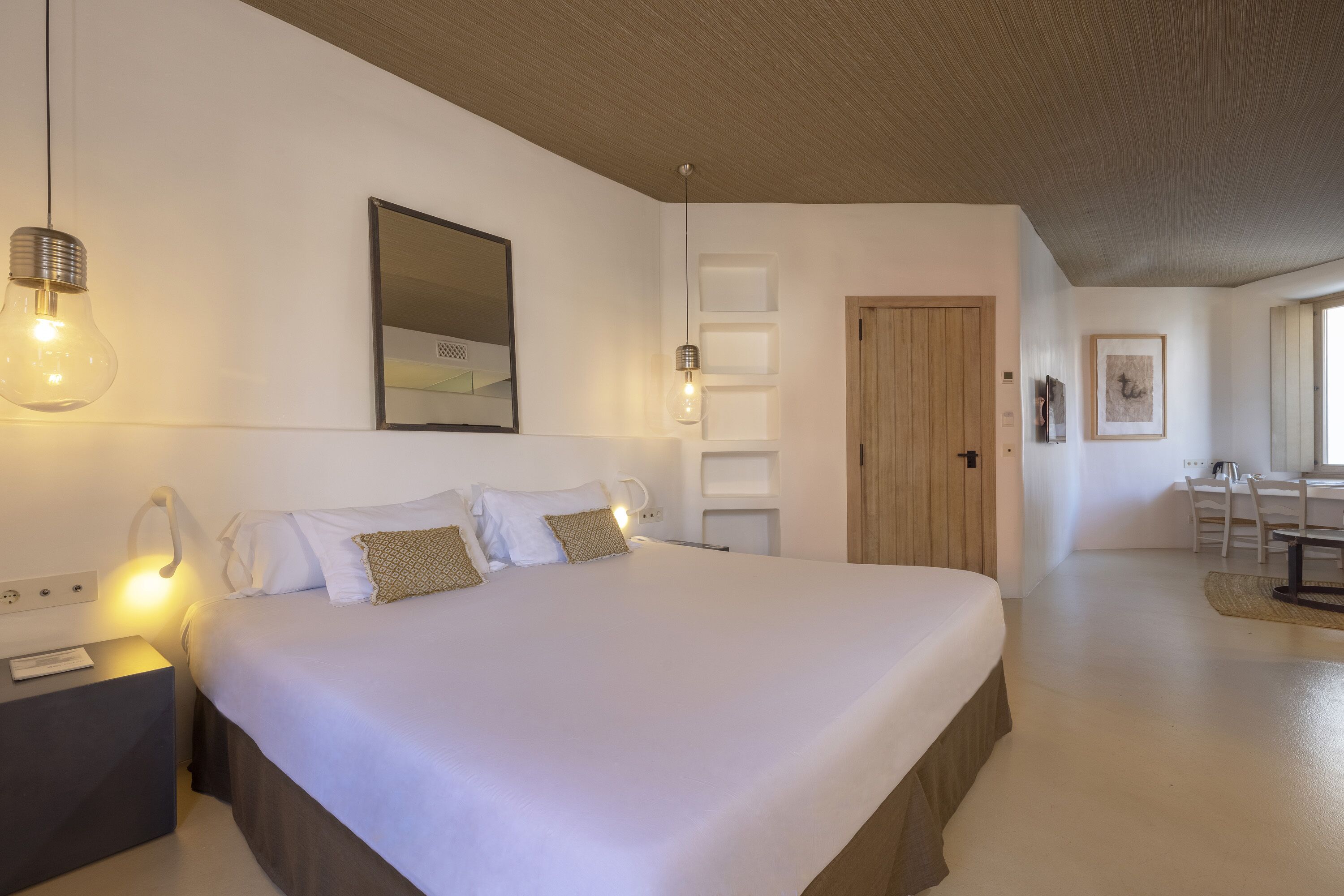 A modern bedroom with a large bed, bedside lamps, a mirror, and a wooden door.
