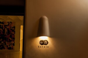 A wall-mounted light fixture with the logo "H&M hotels" and a partial view of a room with a glass door and a framed picture.