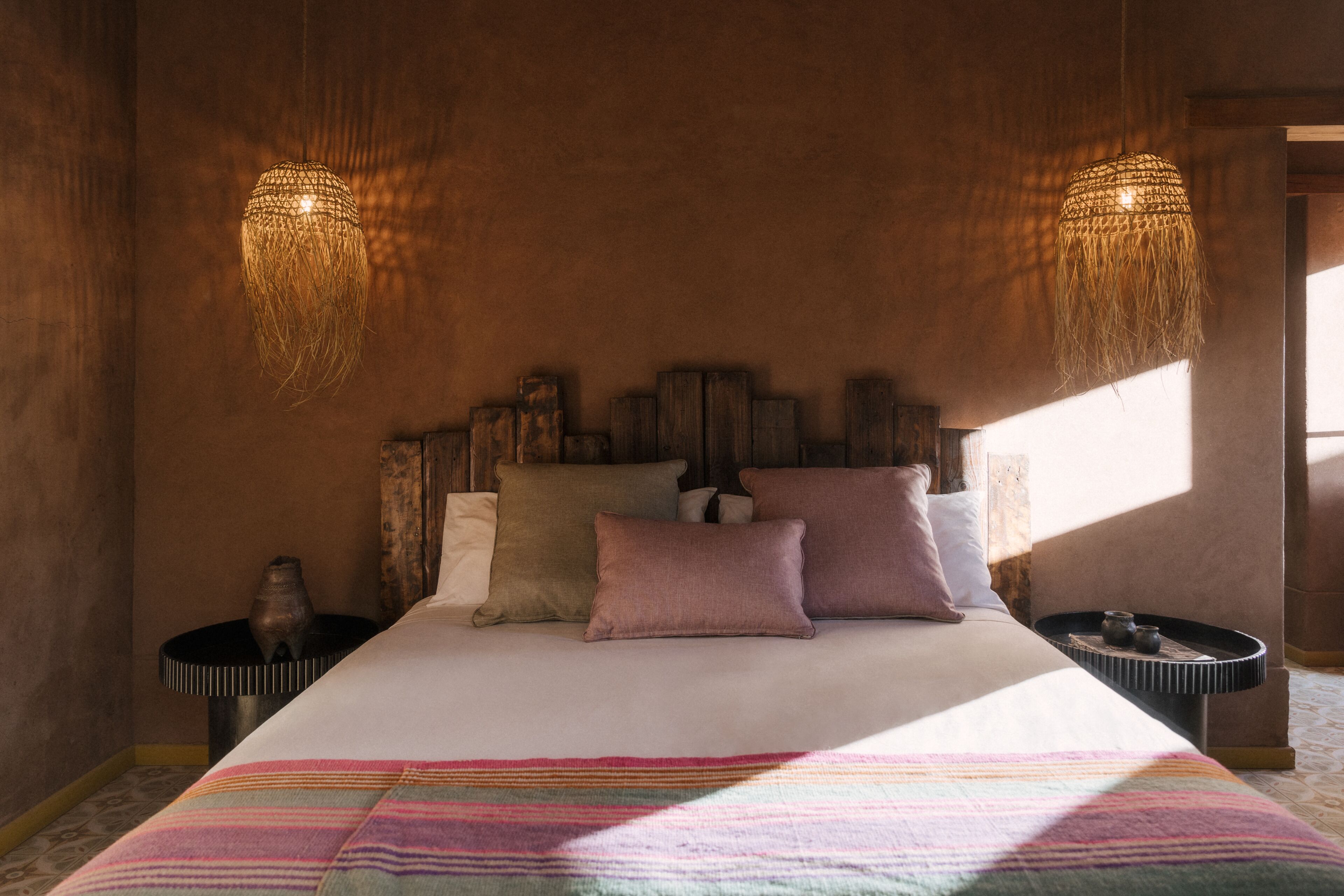 A bedroom with a large bed, two nightstands, a woven light fixture, and a patterned throw blanket.
