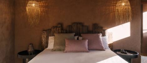 A bedroom with a large bed, two nightstands, a woven light fixture, and a patterned throw blanket.