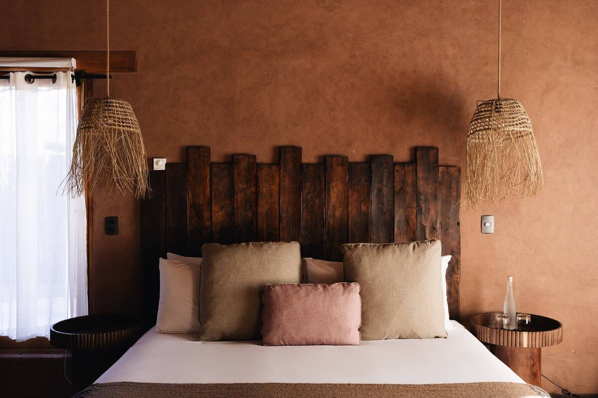 A rustic bedroom with a wooden headboard, a large bed with multiple pillows, and two hanging wicker lamps.