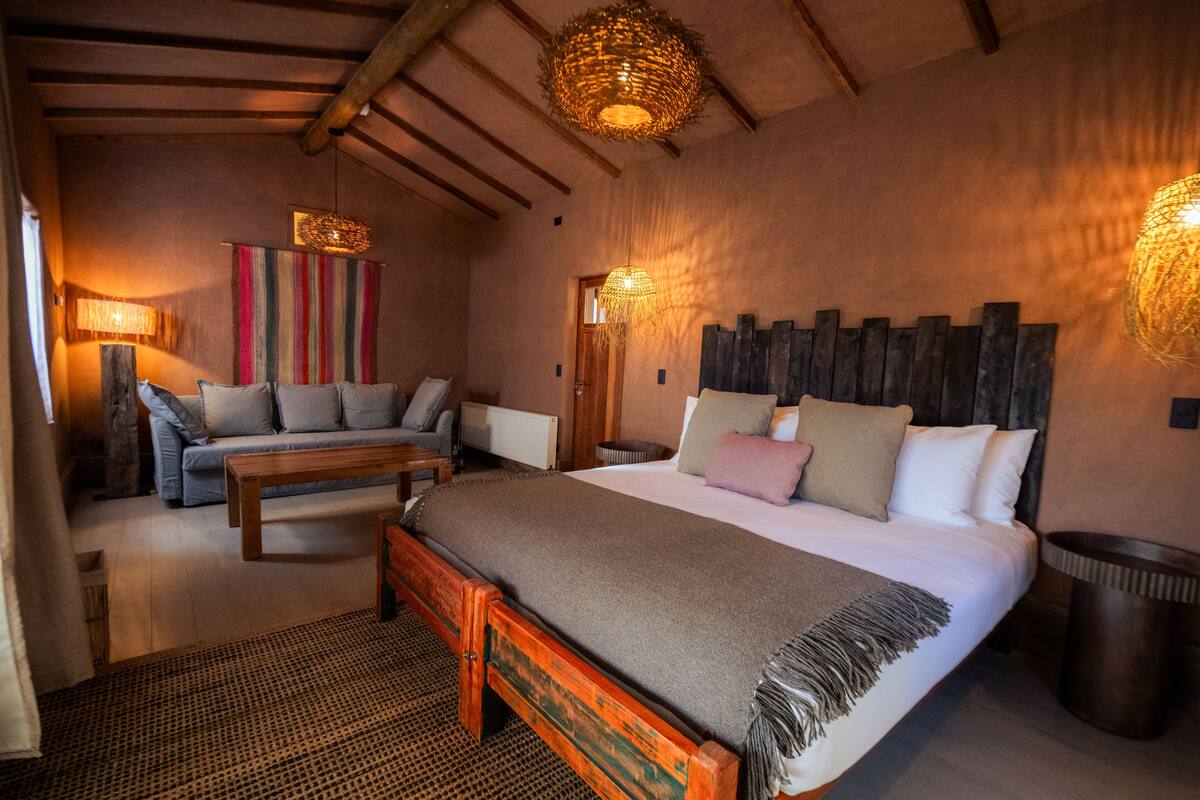 A cozy bedroom with a large bed, a wooden bench, a sofa, and a wall-mounted lamp.