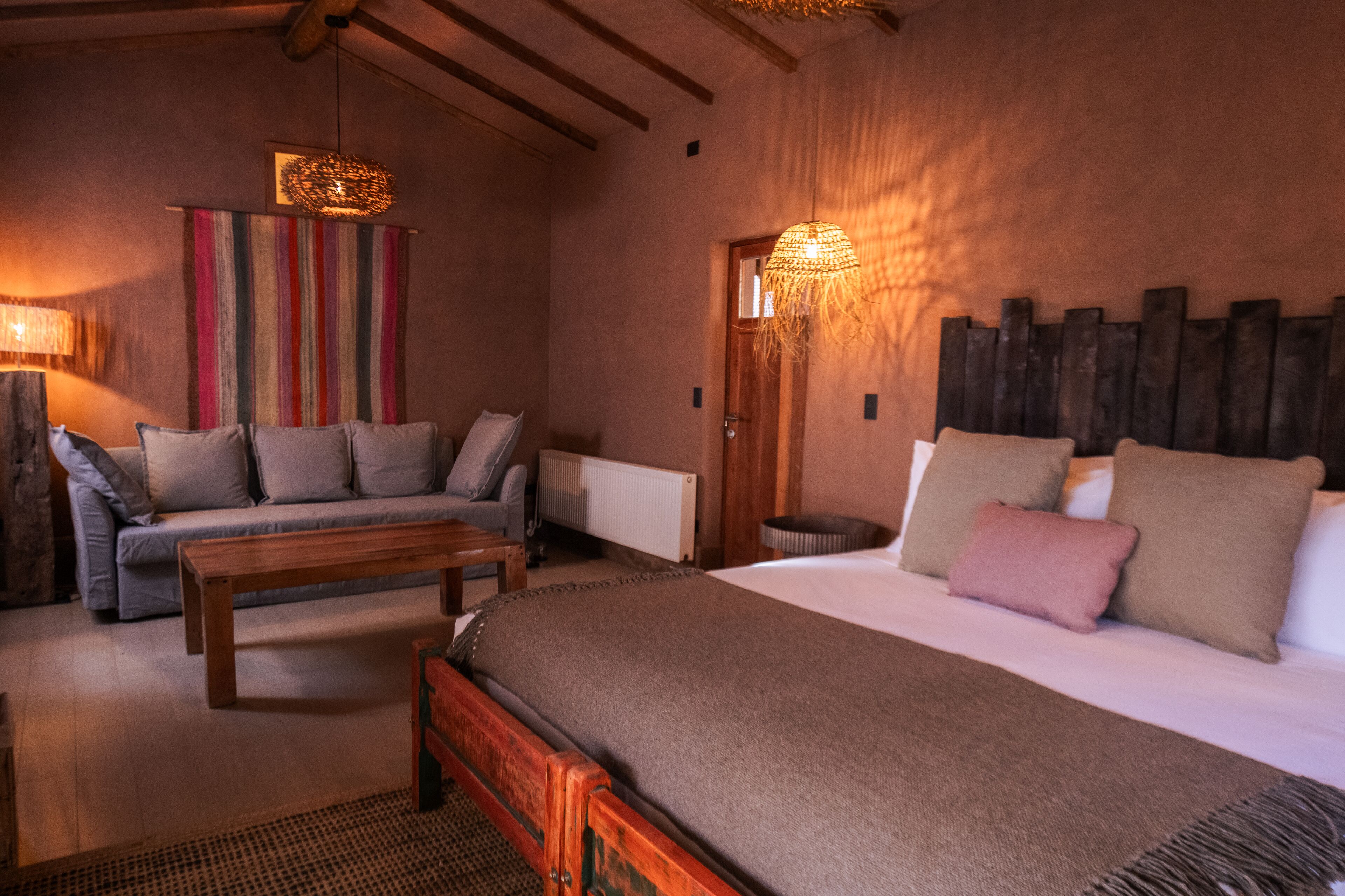 Une chambre confortable avec un grand lit, un canapé et une table basse en bois. On y trouve deux lampes fixées au mur et un rideau rayé aux couleurs vives.