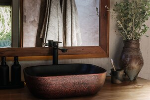 A bathroom with a black vessel sink, a wooden window sill, a towel rack, and a potted plant.