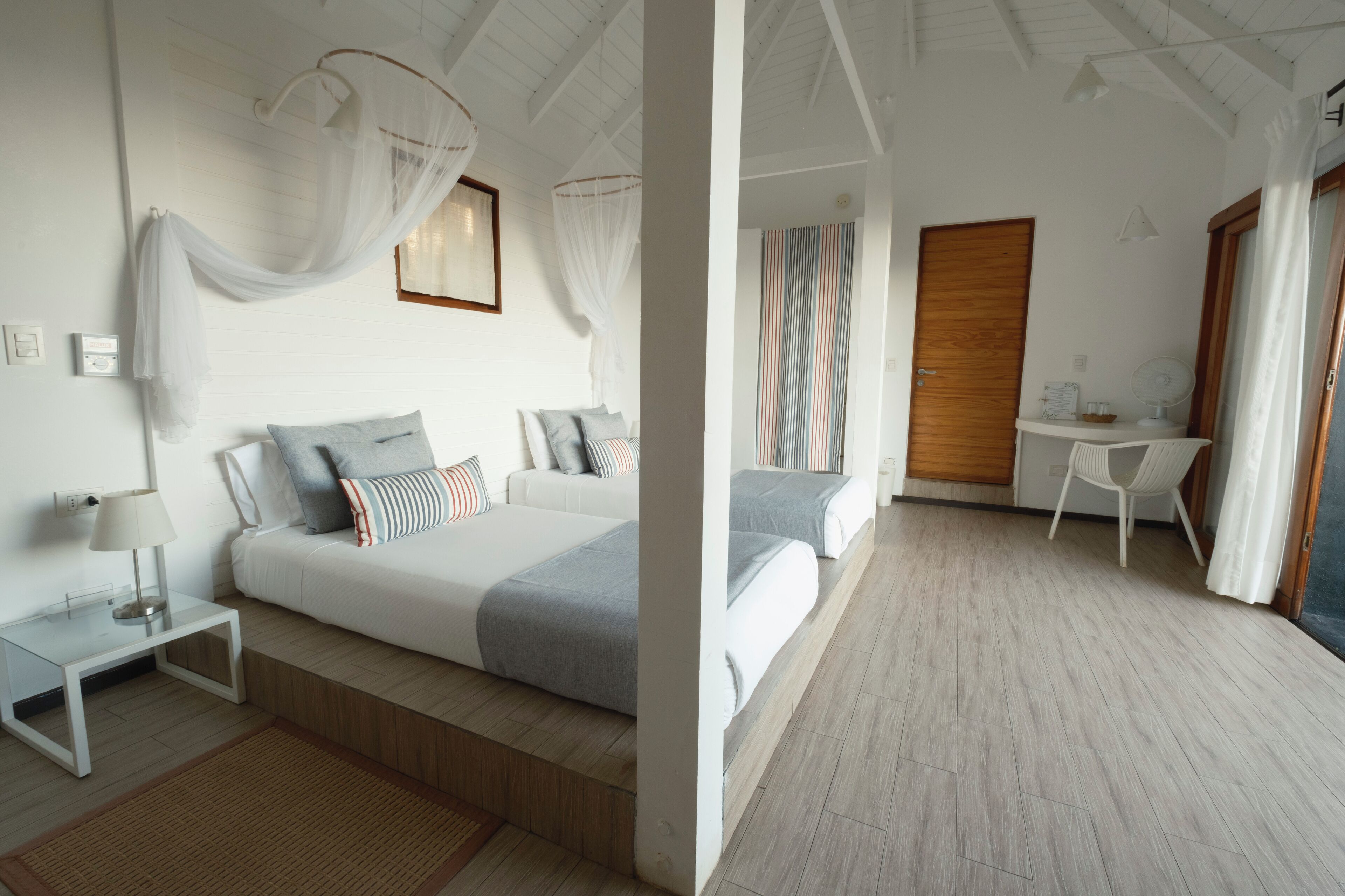 A bedroom with two beds, a bedside table, a lamp, a small desk, and a chair.