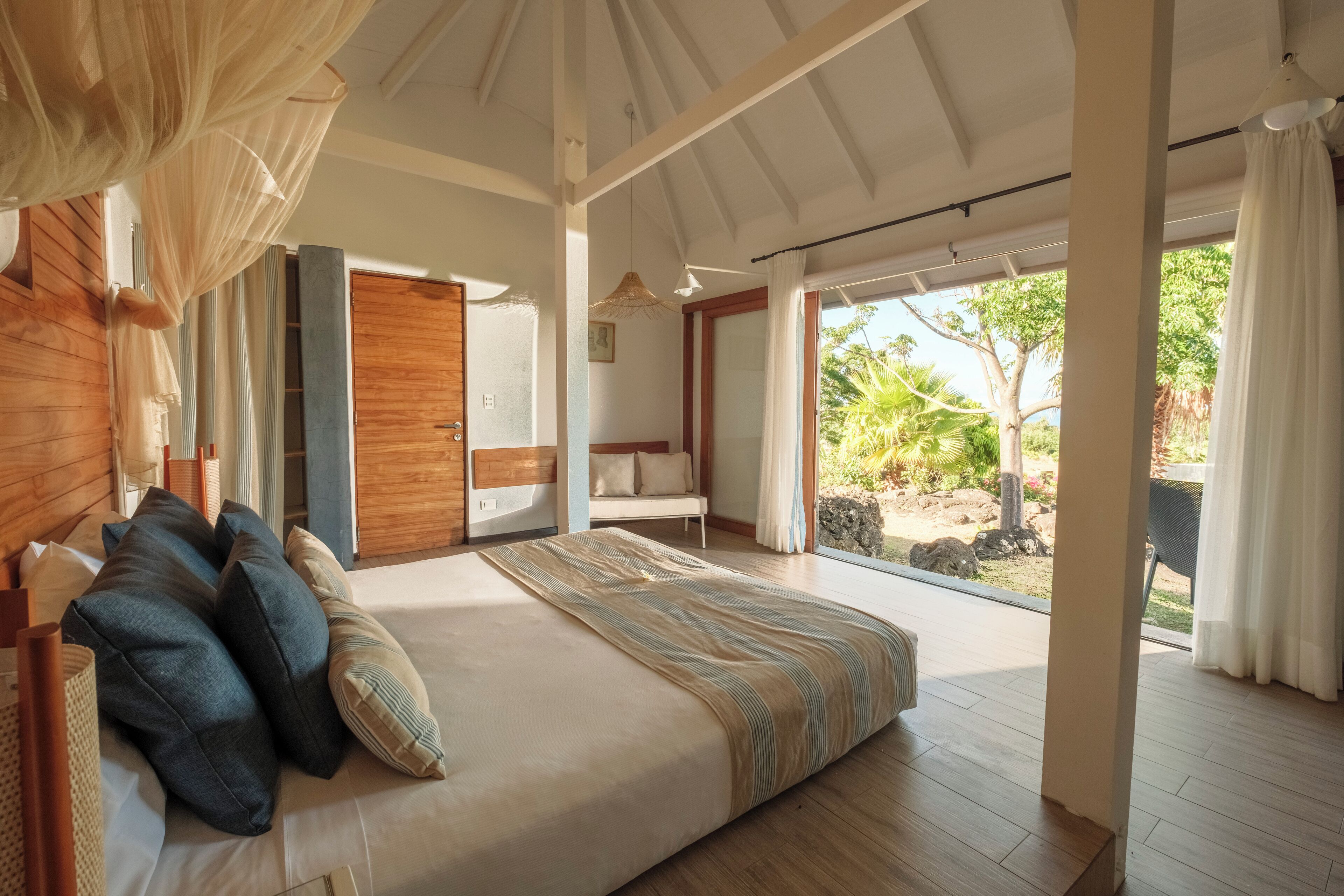 A spacious bedroom with a large bed, wooden headboard, and a view of the garden through large sliding doors.