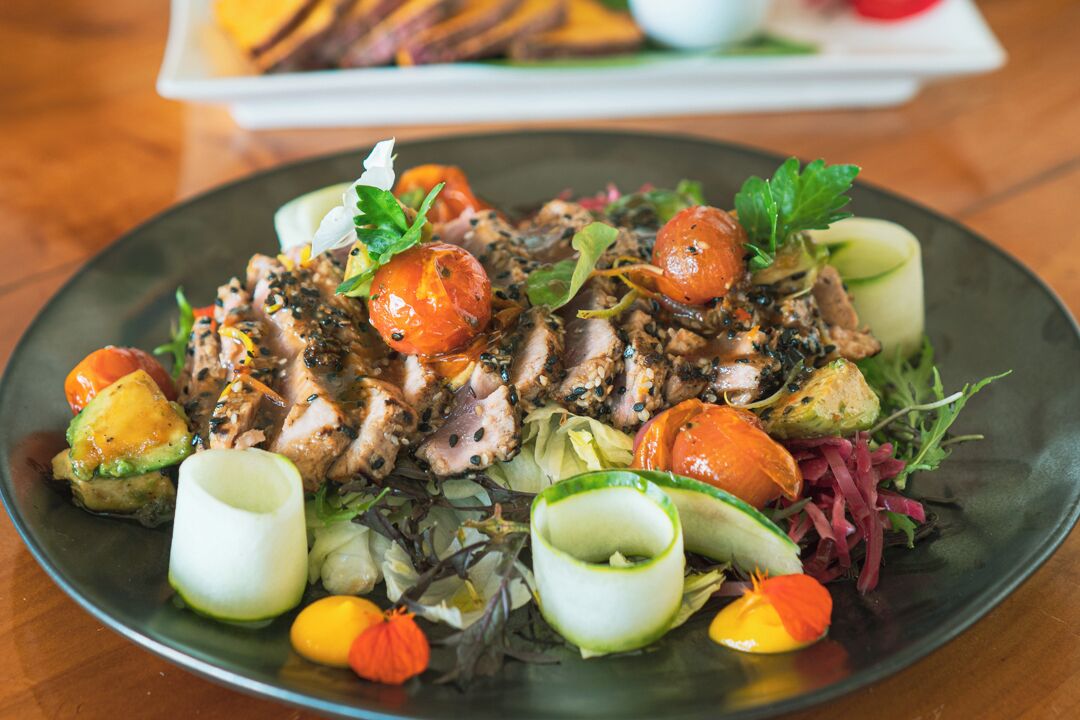 A plate of food with various vegetables and meat, garnished with herbs and edible flowers.