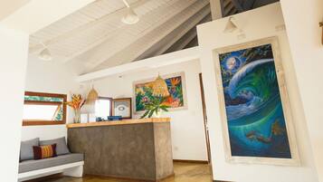 A spacious room with a high ceiling, a wooden paddle, a painting of a wave, and a seating area with cushions.