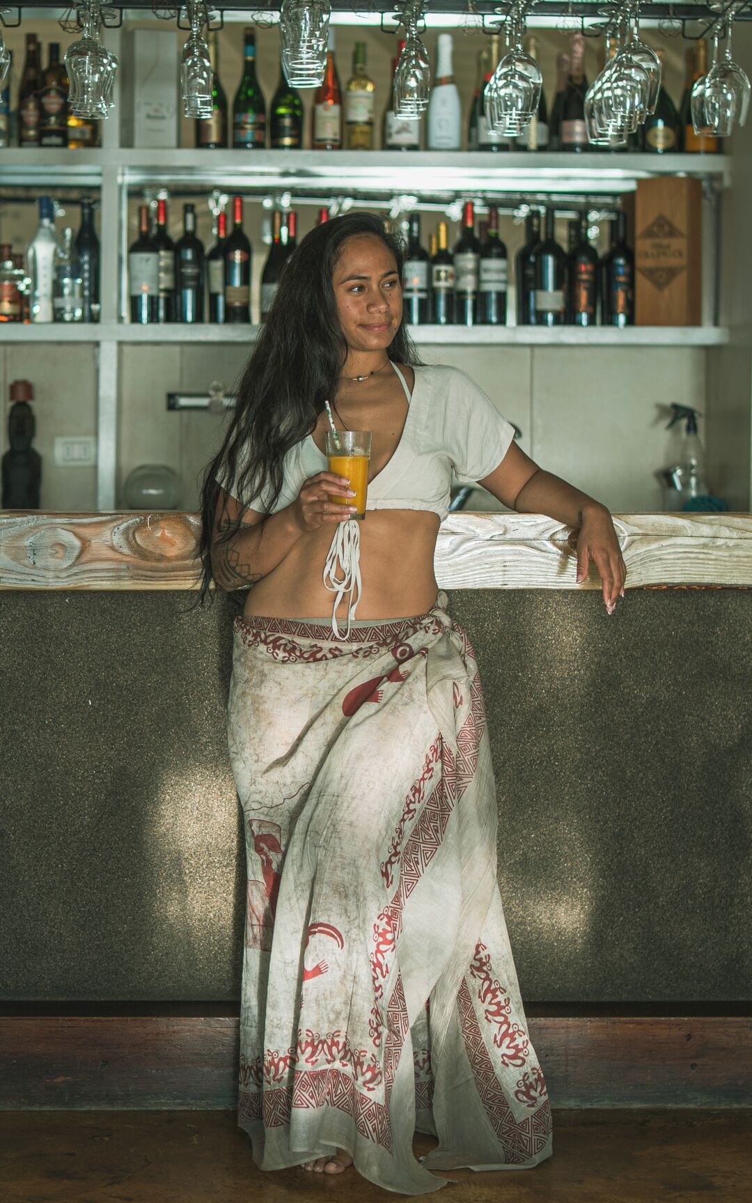Una persona de pie junto a la barra con una bebida, rodeada de estantes llenos de botellas.