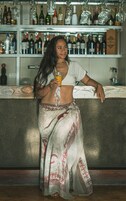 Una persona de pie junto a la barra con una bebida, rodeada de estantes llenos de botellas.