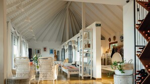 A spacious room with high ceilings, wicker furniture, a central seating area, and a wine rack. - Altiplanico Rapa Nui (Hanga Roa)