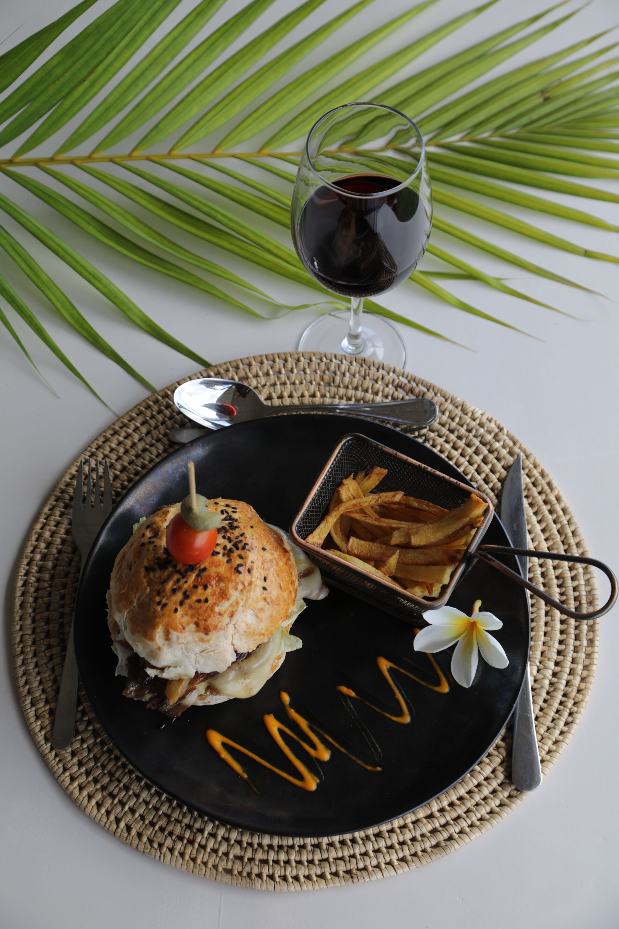 A plate with a sandwich, fries, and a glass of red wine on a woven placemat.