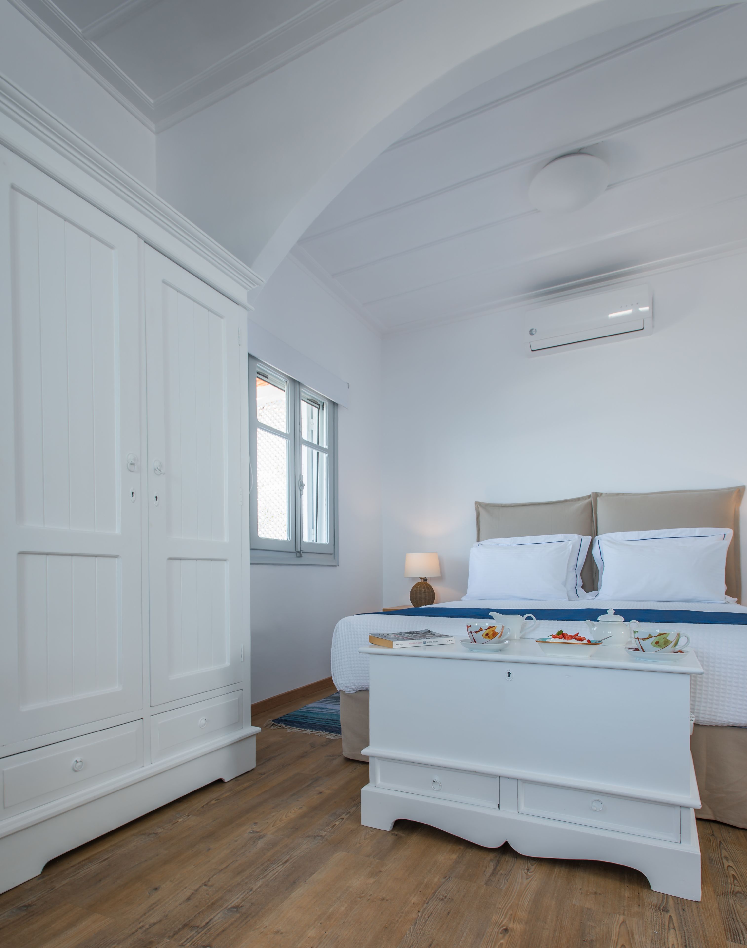 A bedroom with a bed, bedside table, wardrobe, and a window.