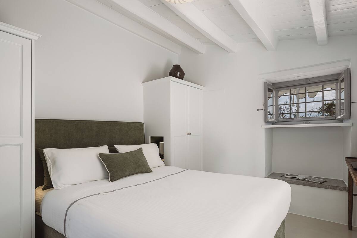 Un dormitorio con cama, mesita de noche, ventana con vistas y puerta.