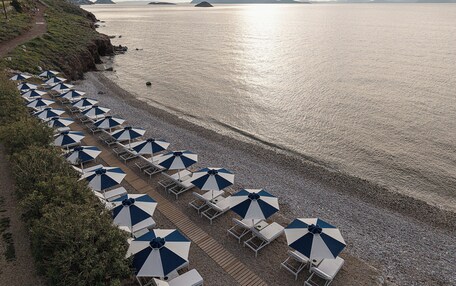 A beach with rows of sun loungers and umbrellas, a rocky shoreline, and distant mountains.