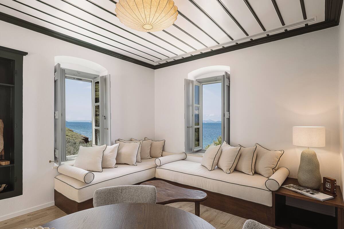 Una sala de estar moderna con un sofá seccional, una mesa redonda y vista al mar a través de amplios ventanales.