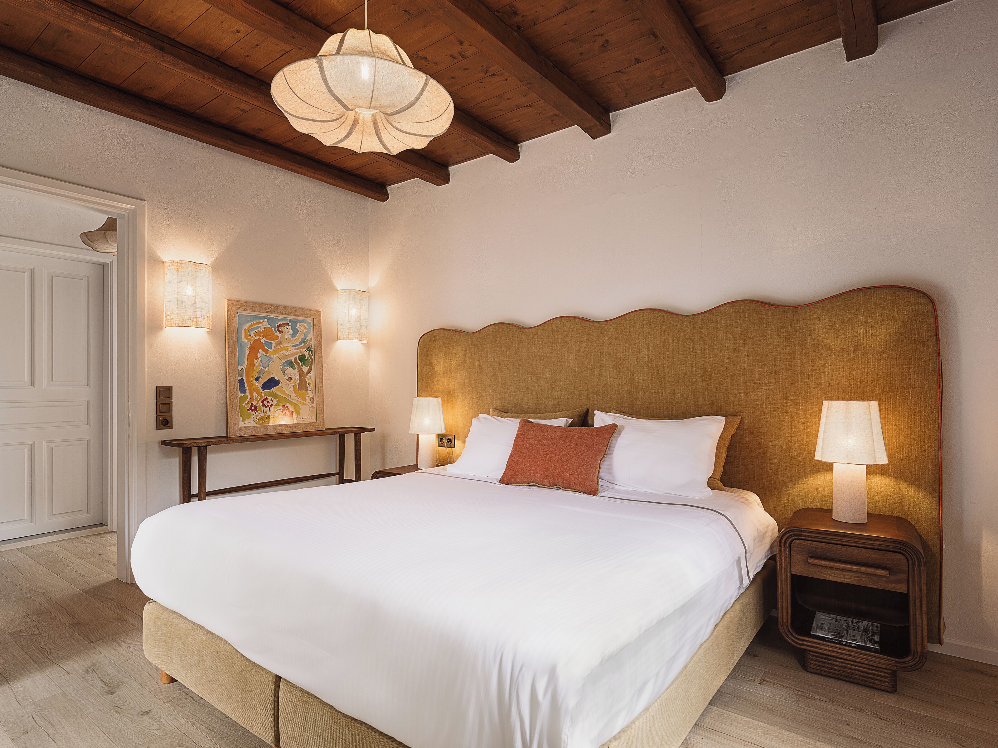 Un dormitorio con una cama grande, cabecera de madera, lámparas de noche y un cuadro en la pared.