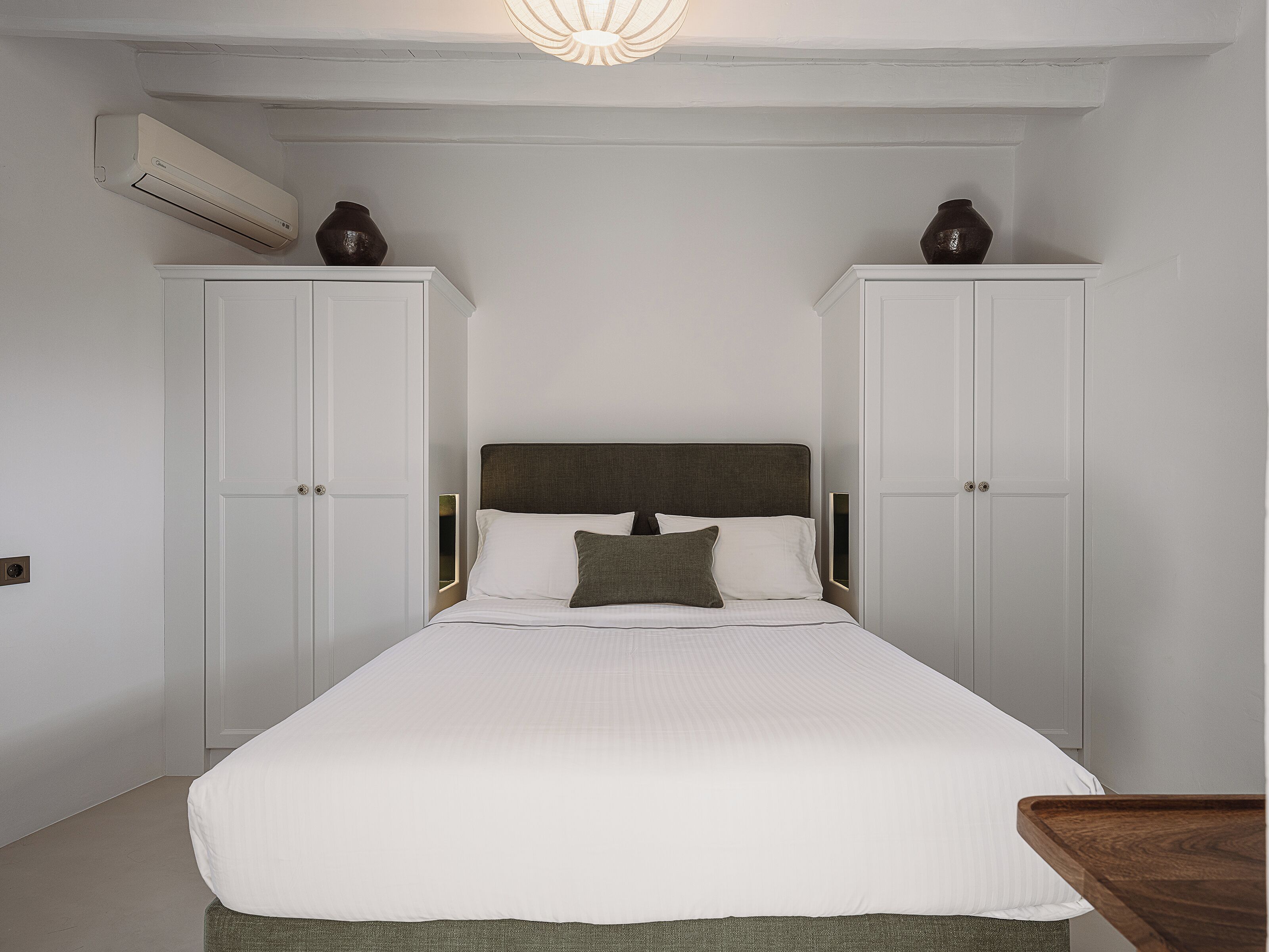 A bedroom with a bed, two wardrobes, and an air conditioning unit.