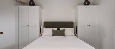 A bedroom with a bed, two wardrobes, and an air conditioning unit.